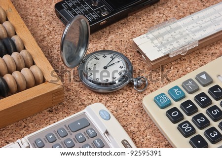 pocket watch, a calculator, a wooden abacus and slide rule on a cork board