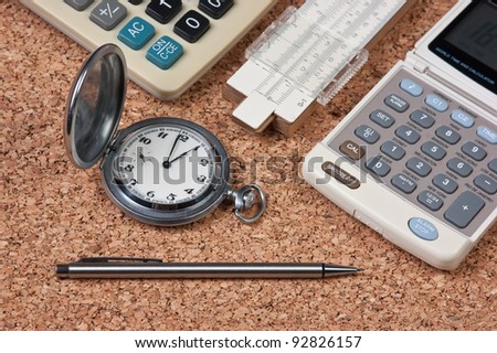 pocket watch,  calculator  and slide rule on a cork board