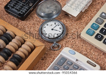 pocket watch, a calculator, a wooden abacus and slide rule on a cork board