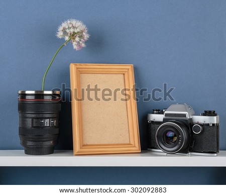 Decorative vases with flower and old camera on white  shelf on blue wallpaper background