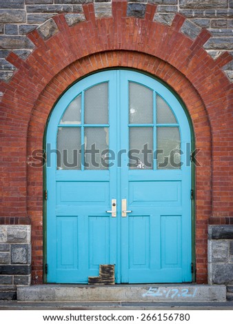 Teal colored wooden door embedded in a red-orange brick and grey stone wall of the Strecker Memorial Laboratory building in Southpoint park on Roosevelt island, New York City.