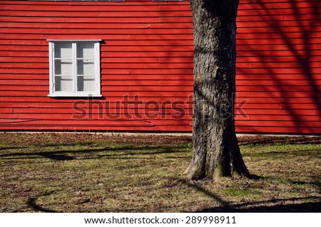 Red wall of scandinavian house with white window and tree near by house