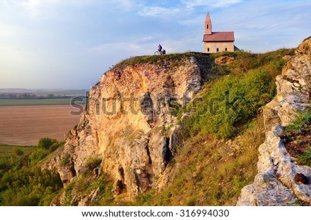 Small man on the bicycle near by old catholic church in slovakia on rocks hill during summer sunset