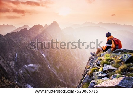 Young male hiker with backpack relaxing on top of a mountain during calm summer sunset - scenery from vacation - photo with space for your montage.