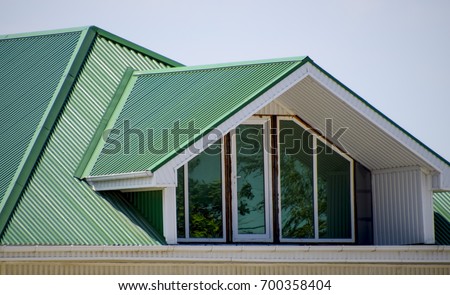 The house with plastic windows and a green roof of corrugated sheet. Roofing of metal profile wavy shape on the house with plastic windows. Green roof of corrugated metal profile and plastic windows.