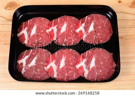Raw beef chuck in black tray on wooden background.