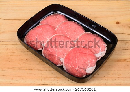 Raw beef sirloin tip in black tray on wooden background.