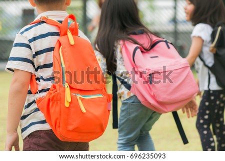 Three pupils of primary school go hand in hand. Boy and girl with school bags behind the back. Beginning of school lessons. Warm day of fall. Back to school. Little first graders.