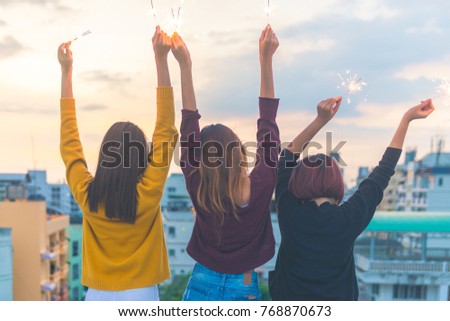 Outdoor shot of young people at rooftop party. Happy group of asia girl friends enjoy and play sparkler at roof top party at evening sunset. Holiday celebration festive party. Teenage lifestyle party.
