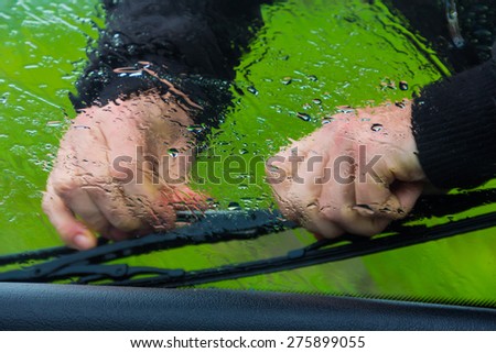 the man in the rain repairs a window wiper by car