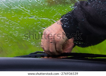 the man in the rain repairs a window wiper by car