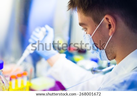 Young scientist during his work with tissue cultures in laminar flow closet in lab