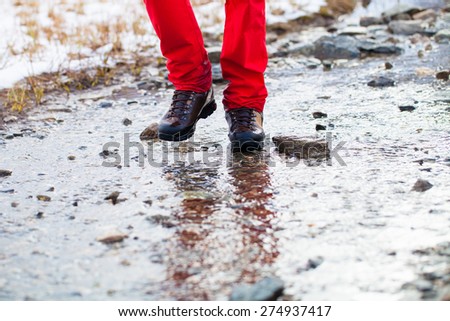Detail of men\'s hiking boots walking through watery footpath in the mountains