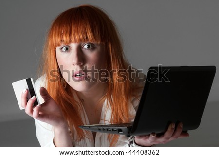 A young scared woman with laptop and credit card in studio
