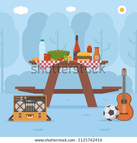 Summer wooden picnic table on forest background. Family barbecue concept with picnic party stuff. Guitar, straw basket, wine and food for outing on public park.