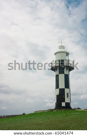 This is lighthouse on green grass and clouds in the background