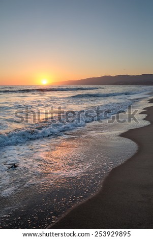 Setting sun next to hills in the distance, on a beach in California.