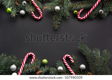 Christmas or New Year decoration background: fir-tree branches, colorful balls, candy on black background with copy space. Top view.
