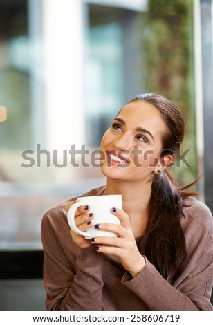 Horizontal image of portrait of happy brunette with mug in hands looking to the corner
