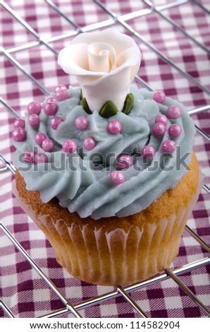 cupcake with blue butter cream, white pink sugar balls and a white rose