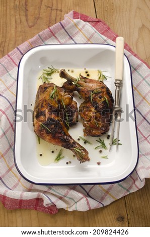 honey glazed chicken leg with olive oil, rosemary, meat fork in an blue and white enamel roasting dish
