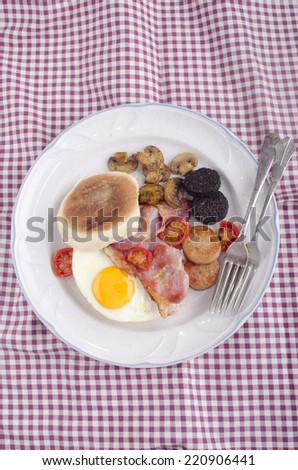 british breakfast muffin with fried egg, black and white pudding, bacon, tomato and mushroom on a plate