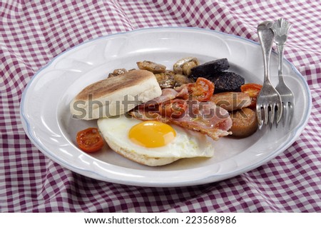 irish breakfast with muffin, black pudding, white pudding, fried egg, grilled cherry tomato and bacon