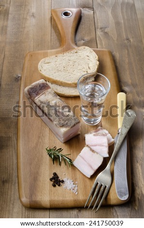 fat bacon with bread, vodka, pepper, coarse salt and rosemary on wooden board