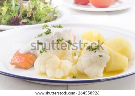 grilled salmon fillet with cheese sauce, jacket potatoes, melted butter and cauliflower on a plate
