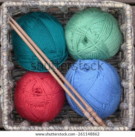 Knitting basket with four balls of colorful balls of yarn and wooden knitting needles
