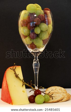Wine glass filled with grapes, surrounded by cheese and crackers