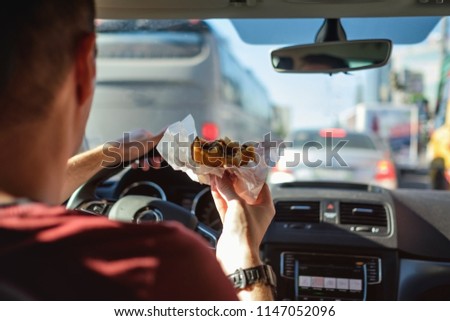 Man driving car while eating hamburger. Waiting and standing in traffic jam