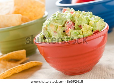 A red bowl filled with guacamole, a green bowl filled with chips and a blue bowl in the background.
