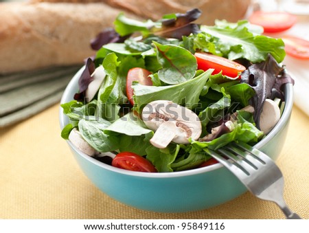 Fresh green salad with mushrooms, tomatoes and bread in the background.