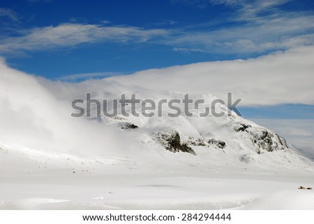 Blue sky, white snow and a veil of low hanging cloud over Norwegian mountains
