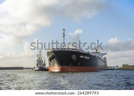 Port of Amsterdam, Noord-Holland/Netherlands - March 27-03-2015 - Motor vessel Medi Venezia is sailing to the quay from OBA. Tugboat Hercules is connected to give push pull assistance. Port side view.