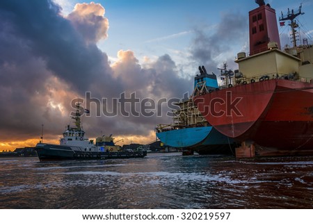 Merchant ships are busy with mooring operations during sunset in port. Beautiful colorful clouds at the background.