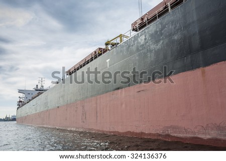 Starboard-side of a huge bulk carrier. Blue clouds at the background of the ship.