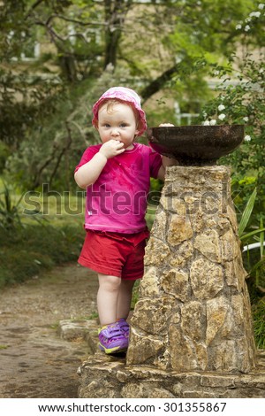 Girl child playing with a small fountain bubbler in the park
