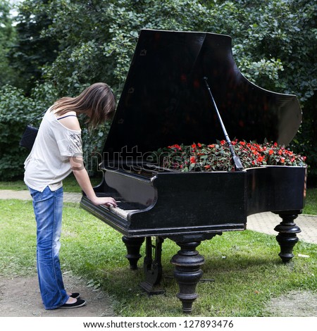 woman playing on an old piano, standing in the garden. The piano is used for landscaping. Inside the piano growing begonia.