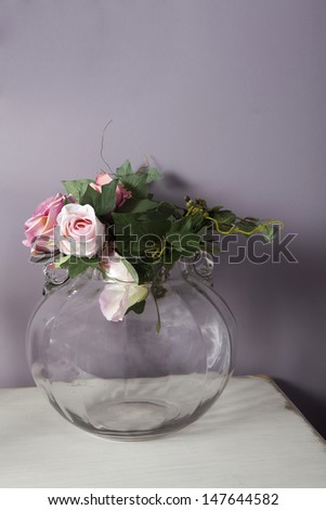 artificial pink and white rose with ivy in glass vase standing on table