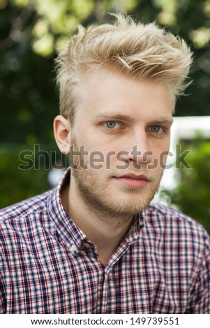 portrait of blond man with blue eyes in check shirt. one who is aware of the latest trends