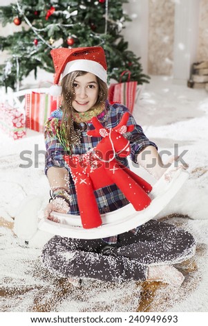 Beautiful young woman in a Santa hat sitting on the floor near Christmas tree