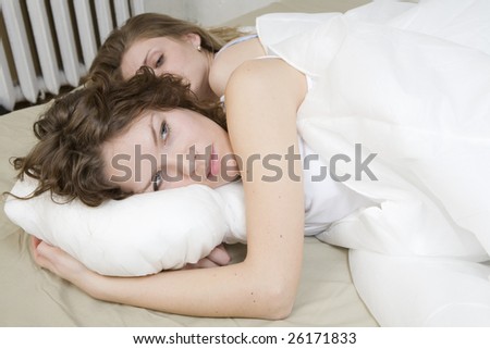 attractive thoughtful brunette curl woman with a pillow on the bed. Two women in bed. Women`s friendship