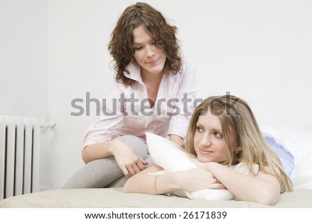attractive thoughtful blond  woman with a pillow on the bed. Her friend sitting near her.  Women`s friendship