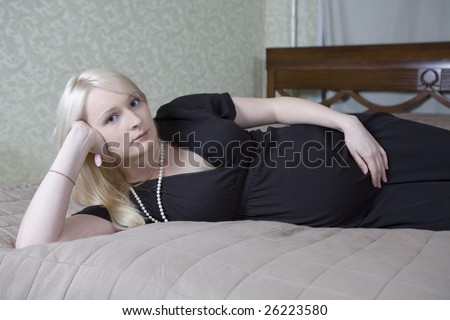Smiling pregnant blond attractive woman holding her belly lying on the bad