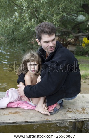 father and daughter sitting on the bank of river. Father hugs daughter. Summer time