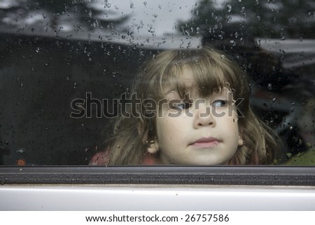 young cute pensive girl looking through window of car. Window covers of rain`s drops