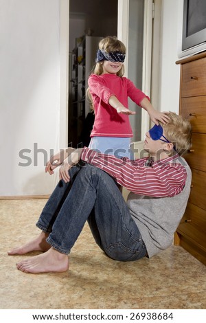 blindfold  sister looking for her brother. Brother with a sleep mask sitting on the floor. They have fun