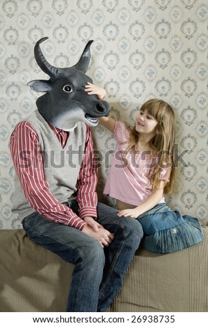 little girl playing with her older brother. Sister wearing diadem . Brother wearing mask of bull. Brother and sister sitting at the sofa